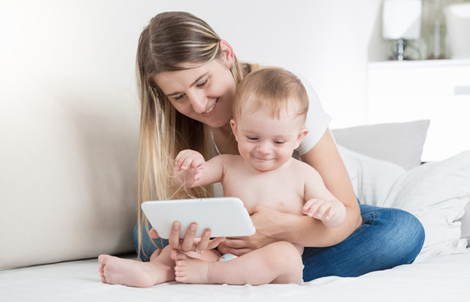 Smiling Young Mother Watching Movie On Tablet Computer With Her